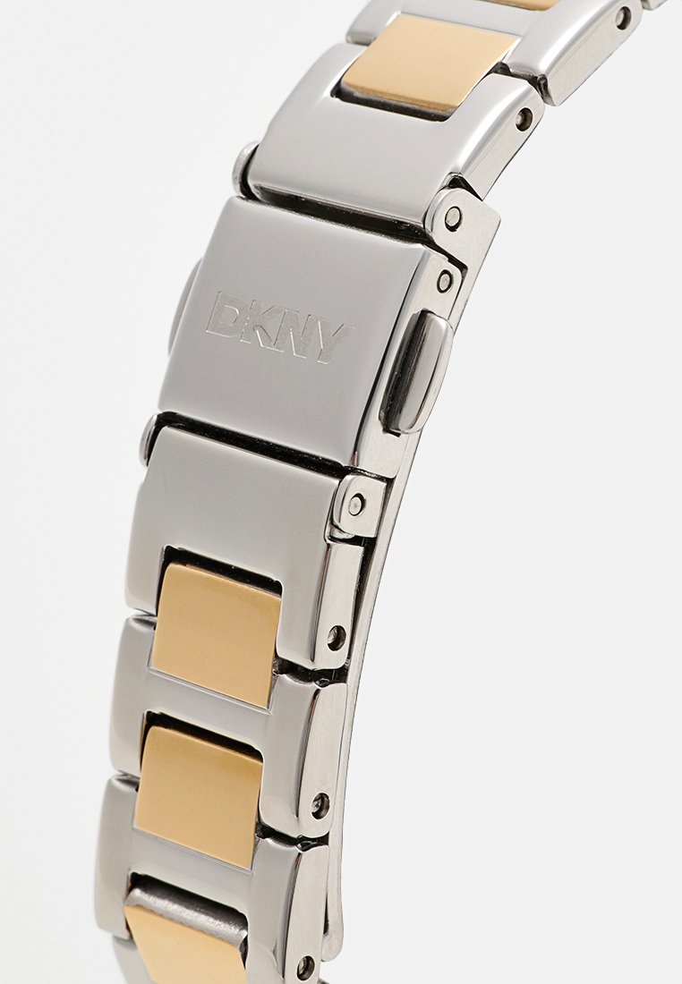 Bracelet de montre en métal argenté et doré avec un design à maillons rectangulaires. Finition polie et logo DKNY sur le fermoir.