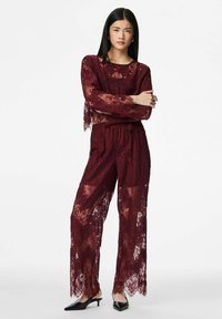 Vīnsarkanā mežģīņu divdaļīgā komplekta komplekts ar garām piedurknēm un vaļīgām biksēm, rotāts ar ziedu rakstiem un viļņotām malām.