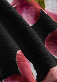 Tessuto nero con grandi motivi floreali astratti nelle tonalità di rosa e verde, dotato di una texture spiegazzata e una finitura morbida.