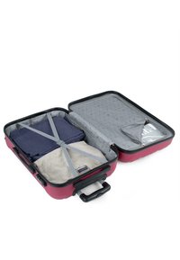 Maleta rígida en burdeos con interior gris. Contiene ropa empacada asegurada por correas elásticas. Presenta un compartimento con cremallera.