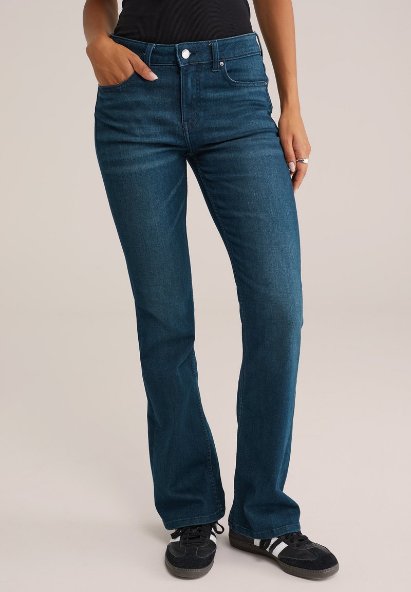 Modre jeans hlače iz denima z visokim pasom, ozkim krojem in razširjenimi hlačnicami. Imajo sprednje žepe in gumbasto zapiranje. Tkanina z teksturo in subtilnim zbledelostjo.