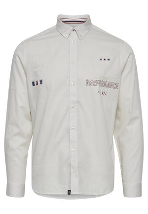 Bijela košulja s dugim rukavima, ukrašena vezenim detaljima i kontrastnim prugama na ovratniku. Natpis uključuje "Autentična PERFORMANSA."