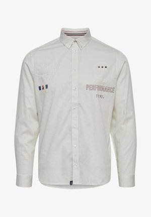 Fehér, hosszú ujjú ing, hímzett részletekkel és kontrasztos csíkokkal a galléron. A felirat: "Eredeti TELJESÍTMÉNY."