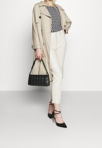 Cappotto trench beige, top a fantasia, pantaloni bianchi, borsa a tracolla nera e scarpe col tacco nere con cinturini alla caviglia. Un completo elegante.
