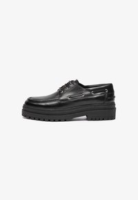 Zapatos de cuero negro con un diseño aerodinámico, que cuentan con ojales metálicos, suela de goma gruesa y acentos texturizados.