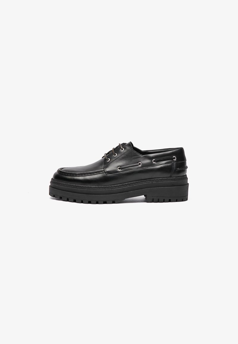 Schwarze Lederschuhe mit einem stromlinienförmigen Design, ausgestattet mit Metallösen, dicker Gummisohle und strukturierten Akzenten.