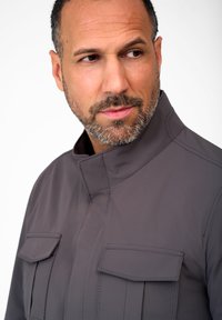 Gray, waterproof jacket with a high collar, two large chest pockets, and visible stitching details. Smooth texture, modern design.