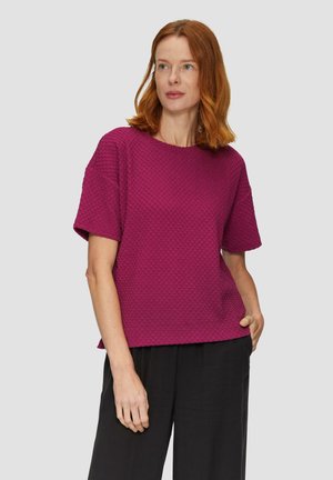 Haut magenta à manches courtes avec un design texturé et à motifs ; col rond et coupe décontractée, associé à un pantalon noir.