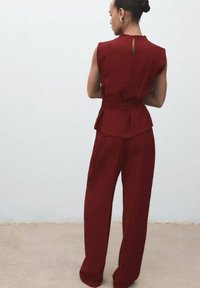 Burgundský dvoudílný outfit skládající se z topu bez rukávů a kalhot s širokými nohavicemi. Top má ozdobu peplum a otvor na zádech ve tvaru klíčky.
