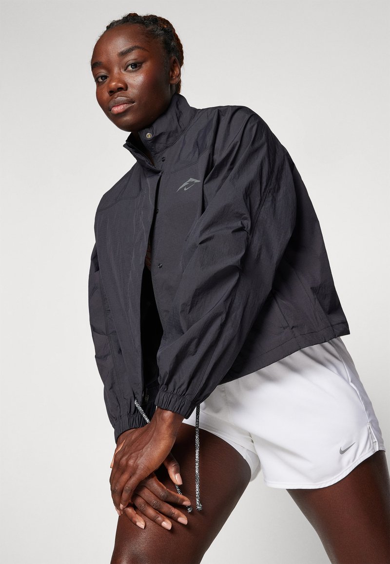 Schwarze, leichte, kurz geschnittene Jacke mit hohem Kragen, elastischen Bündchen und verstellbaren Kordeln. Mit einem dezenten Logo auf der Brust.