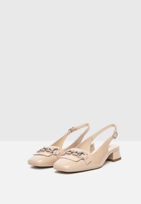 Beige patent leather slingback shoes with a rounded toe, low block heel, and decorative silver chain accents on the front.