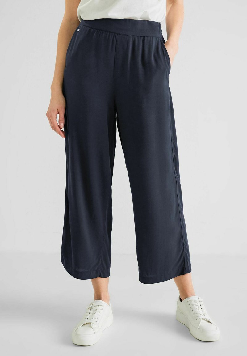Marineblaue +weiter Hosen mit elastischem Bund, aus glattem Stoff, mit seitlichen Taschen und kombiniert mit weißen Sneakern.