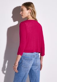T-shirt fuchsia à manches longues avec un col rond et des poignets froncés, associé à un jean en denim bleu clair avec des poches arrière et une coupe décontractée.