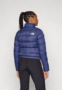 Námornícka modrá prešívaná bunda s vysokým golierom, prešívaným vzorom a elastickými manžetami. Obsahuje logo na hornej časti chrbta a skrátenú siluetu.