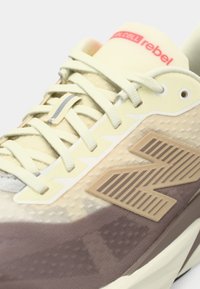 Light-colored athletic shoe with textured mesh upper, beige and brown accents, rubber sole, and visible logo on the side and tongue.