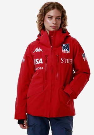 Giacca impermeabile rossa con cappuccio, dotata di due tasche con zip, dettagli con logo e polsini regolabili. Dettagli riflettenti sulla parte anteriore.