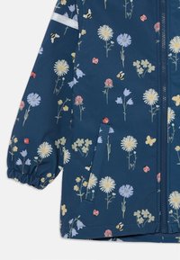 Marineblå vandtæt jakke med blomstermønster, der indeholder mælkebøtter, kløver og insekter. Elastiske manchetter og lynlåslomme detalje.