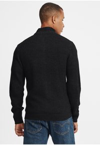 Maglione nero a costine con colletto alto, maniche aderenti e tessuto testurizzato, abbinato a jeans in denim blu.