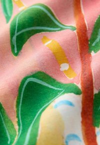 Tela colorida con un fondo rosa que presenta hojas verdes y acentos amarillos, mostrando una textura suave y un patrón acuarelado.