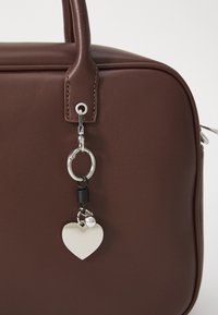 Brown faux leather handbag featuring a silver hardware charm with a heart shape and keyring attachment. Smooth texture, structured design.