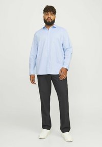Lichtblauw overhemd met lange mouwen en een knoopjeskraag, gecombineerd met donkergrijze broek en witte sneakers; zachte stof, ontspannen pasvorm.