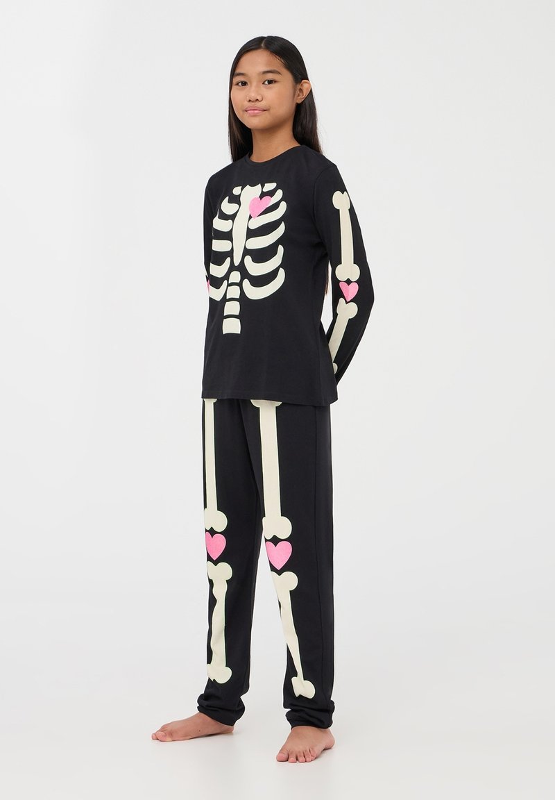 Czarny komplet piżamy z motywem szkieletonu w kremowym kolorze z różowymi akcentami w kształcie serc. Długi rękaw i pasujące spodnie w luźnym fasonie.