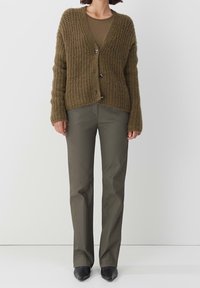 Brun stickad cardigan med djup V-hals, med knappstängning och oversized ärmar, i kombination med olivgröna slim-fit byxor och svarta skor.