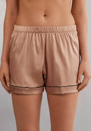 Middenstuk van een persoon die glanzende beige zijden shorts draagt met een elastische tailleband en zwarte bies vlakbij de zoom.