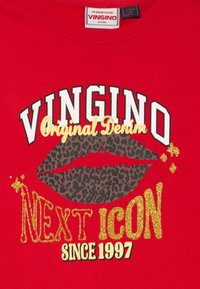 T-shirt rossa in cotone con grande scritta "VINGINO" e design di labbra a stampa leopardata, dettagli con glitter dorati e la dicitura "NEXT ICON SINCE 1997".