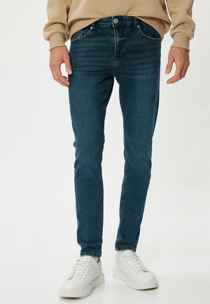 Ciemnoniebieskie dżinsy o slim fit, pięć kieszeni, z przodem z guzikami i zamkiem, zestawione z białymi sneakersami.