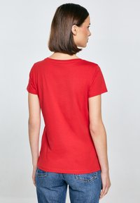 Červené tričko s krátkým rukávem z měkké bavlny, s klasickým kulatým výstřihem a uvolněným střihem, kombinováno s modrými džíny.