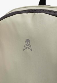 Tejido de mochila verde claro con un acabado mate, que presenta un logo de calavera y huesos cruzados en gris y acentos de cremallera en gris oscuro.