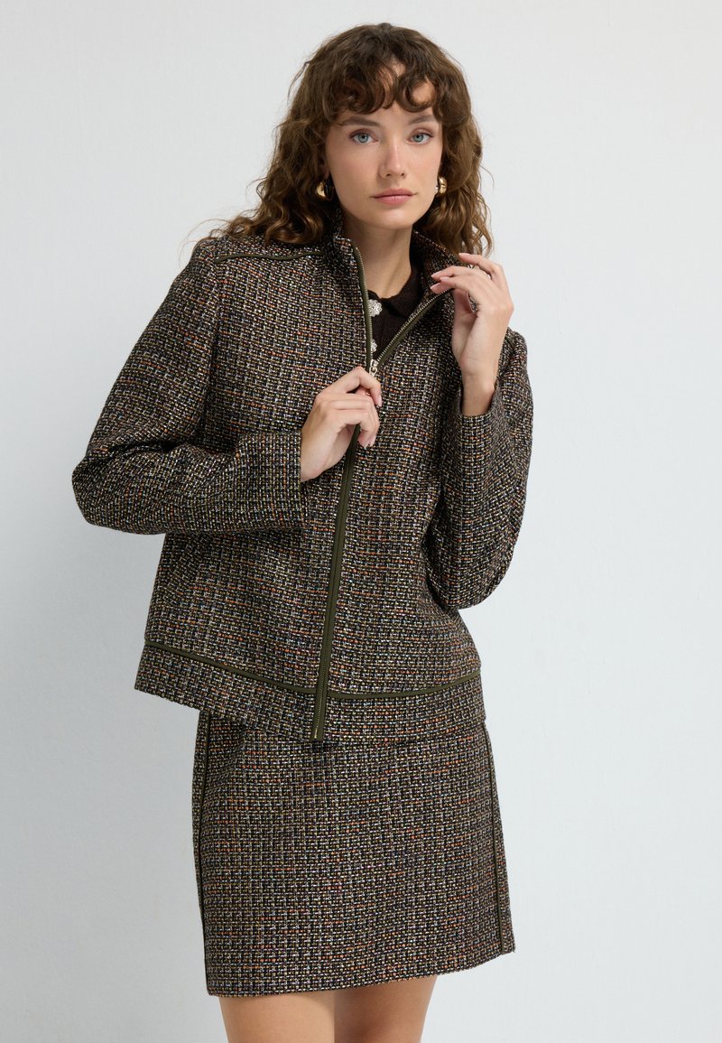 Veste marron texturée avec fermeture éclair à l'avant et jupe assortie, présentant un motif à carreaux en fils multicolores et une coupe décontractée.