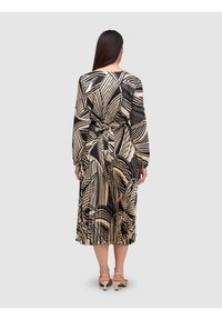 Robe à motifs noir et beige avec manches longues, une ceinture à la taille, et une jupe fluide, ornée de motifs ressemblant à des feuilles.