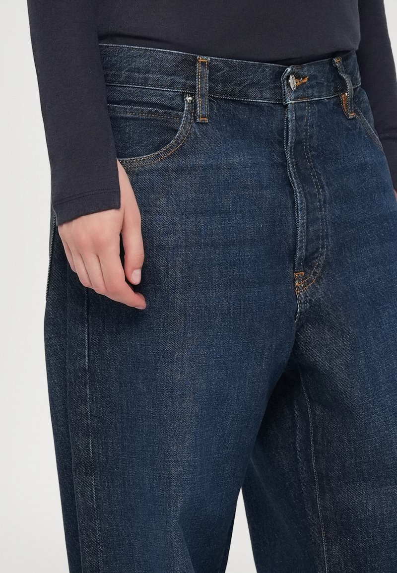 Dunkelblaue Denim-Jeans verfügen über ein gerades Bein-Design mit einem Knopf- und Reißverschluss sowie sichtbaren Nähakzenten an den Taschen.