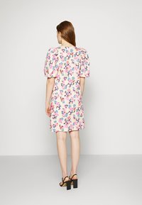 Vestido florido com mangas bufantes em cores pastel sobre um fundo claro. Comprimento curto, detalhe nas costas inclui uma costura sutil e decote redondo.