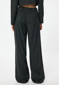 Pantalons larges gris charbon, confectionnés dans un tissu texturé, dotés d'une taille avec passants de ceinture et de détails plissés à l'avant.