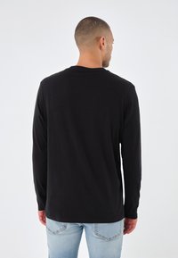 Black long-sleeve t-shirt in a smooth cotton blend, featuring a round neckline and slightly curved hem, paired with light blue jeans.
