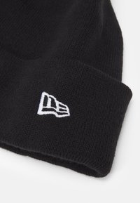 Gorro de punto negro con un logotipo bordado en blanco en el puño vuelto. Textura suave con un diseño ajustado.