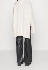 Beige geribbelde trui in oversize met zijsplitten, gecombineerd met zwarte leren flarebroeken en stevige zwarte laarzen.