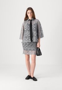 Spitzenkleid-Set mit einem transparenten Design in Grau, ausgestattet mit einer schwarzen Krawatte und kurzen Ärmeln. Begleitet von einer kleinen schwarzen Handtasche und flachen Schuhen.
