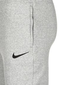 Pantalones de chándal grises hechos de una suave mezcla de algodón con un logo negro de Nike en el muslo izquierdo y bolsillos laterales. Diseño ajustado con cinturilla elástica.
