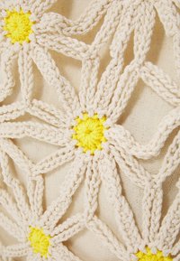 Design floral en crochet avec du coton beige, présentant des centres jaunes. Le motif est composé de pétales entrelacés formant une surface texturée.