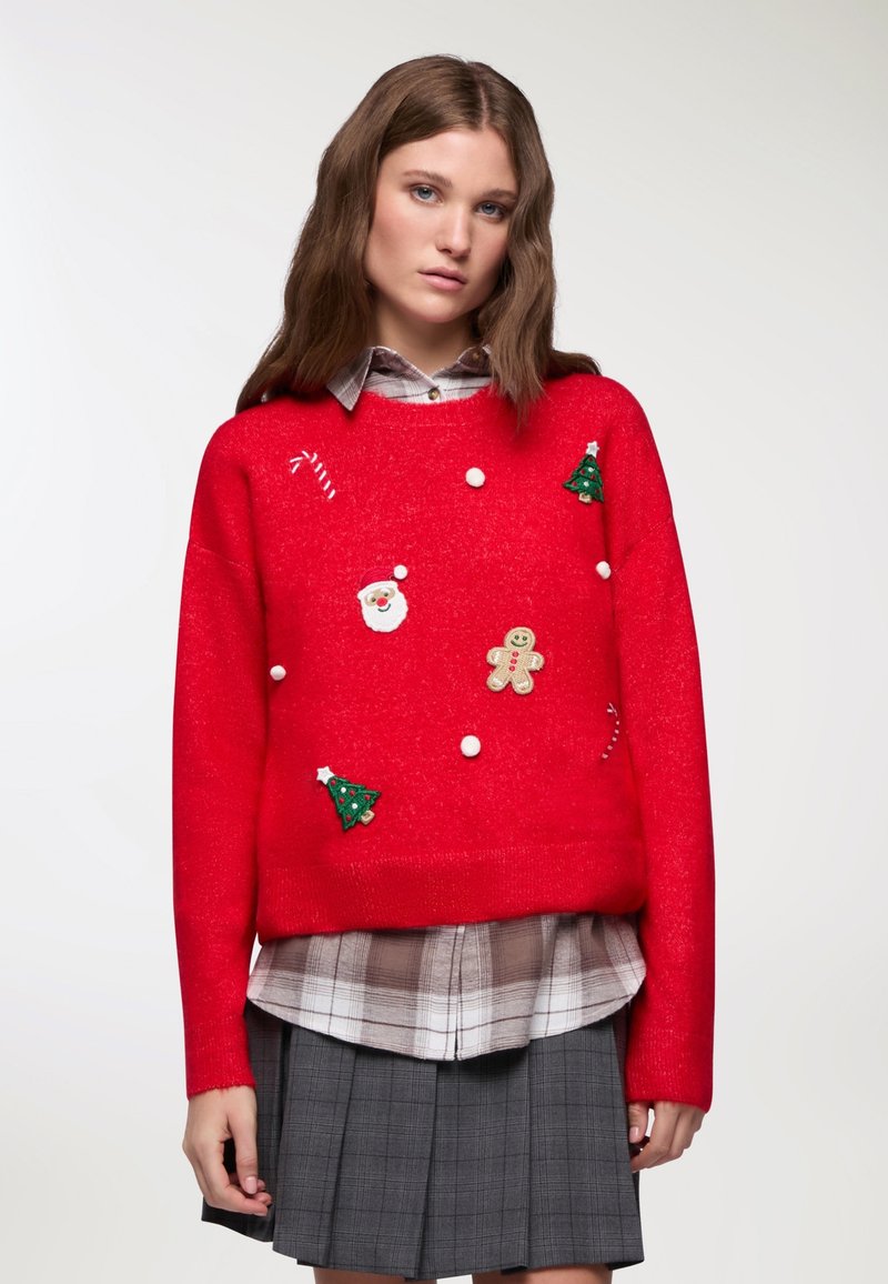 Czerwony sweter robiony na druty z świątecznymi ozdobami: Mikołaj, piernikowy ludzik, choinki i pompony. Nałożony na koszulę w kratę i spódnicę.