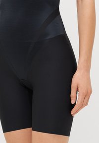 Black high-waisted shapewear shorts with a smooth, stretchy texture, featuring a mid-thigh cut and a functional button detail at the front.