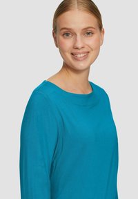 Turkooise lange mouwen top met een ronde halslijn. Zacht, gladde stof met minimale naden voor een schone uitstraling.