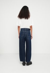 Calças de ganga escuras de perna larga com cintura alta, com dois bolsos traseiros e detalhe costurado. Combinadas com uma t-shirt branca de corte largo.