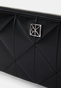 Čierna kožená peňaženka s prešívaným vzorom, striebornými doplnkami a zipsovým uzatváraním. Hladký povrch s geometrickým dizajnom.