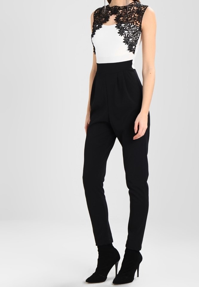 Bodysuit en dentelle noire avec panneaux en dentelle, haut blanc, pantalons noirs taille haute et bottines noires, présentant une silhouette ajustée et une texture lisse.