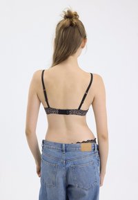 Reggiseno a stampa leopardata nera con spalline regolabili e chiusura a gancio. Indossato con jeans in denim blu a vita alta, con vita testurizzata.